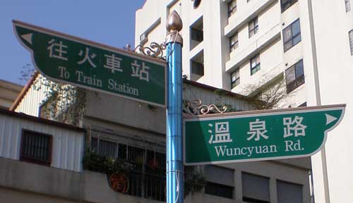 two steet signs atop one pole: one reading 'To Train Station', the other 'Wuncyuan Rd'