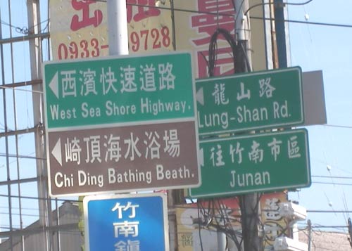 signs reading 'Junan', 'West Sea Shore Highway.', 'Lung-Shan Rd.', and 'Chi Ding Bathing Beath.'