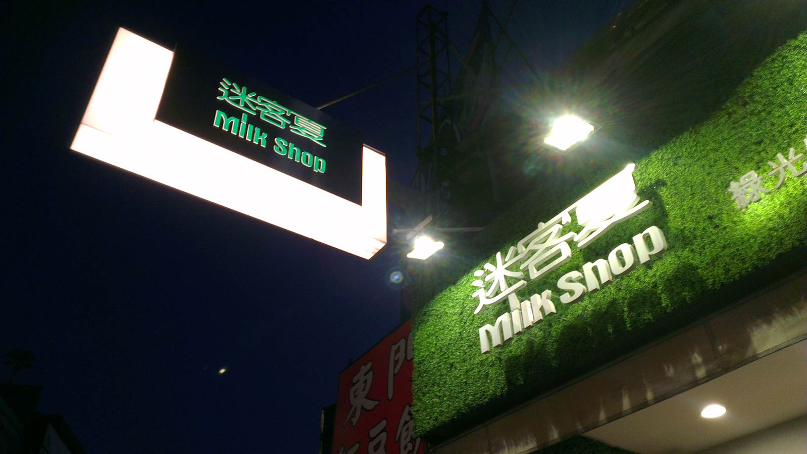 sign for a drinks store, labeled 'milk shop' in English and 'mi ke xia' in Chinese characters