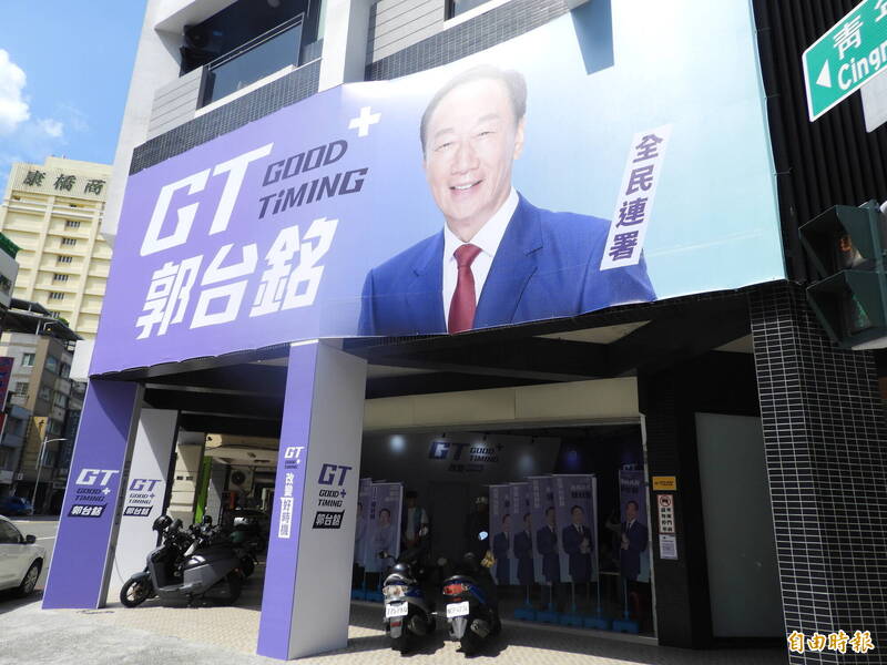 photo of a large poster on a building. It reads 'GT GOOD TiMING 郭台銘' and has a photo of Terry Gou against a blue and purple background